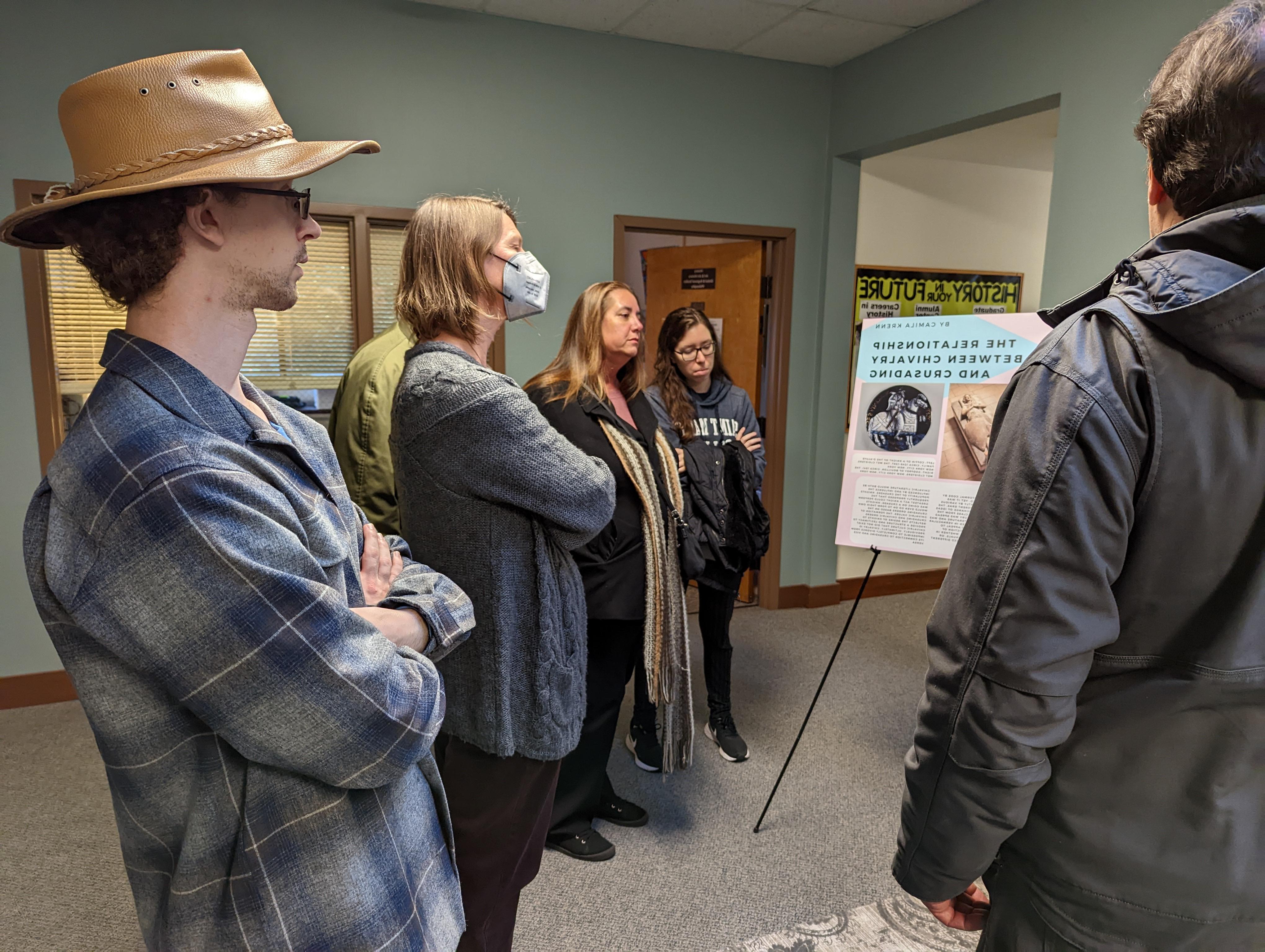 people standing and listening to a student talk about their thesis