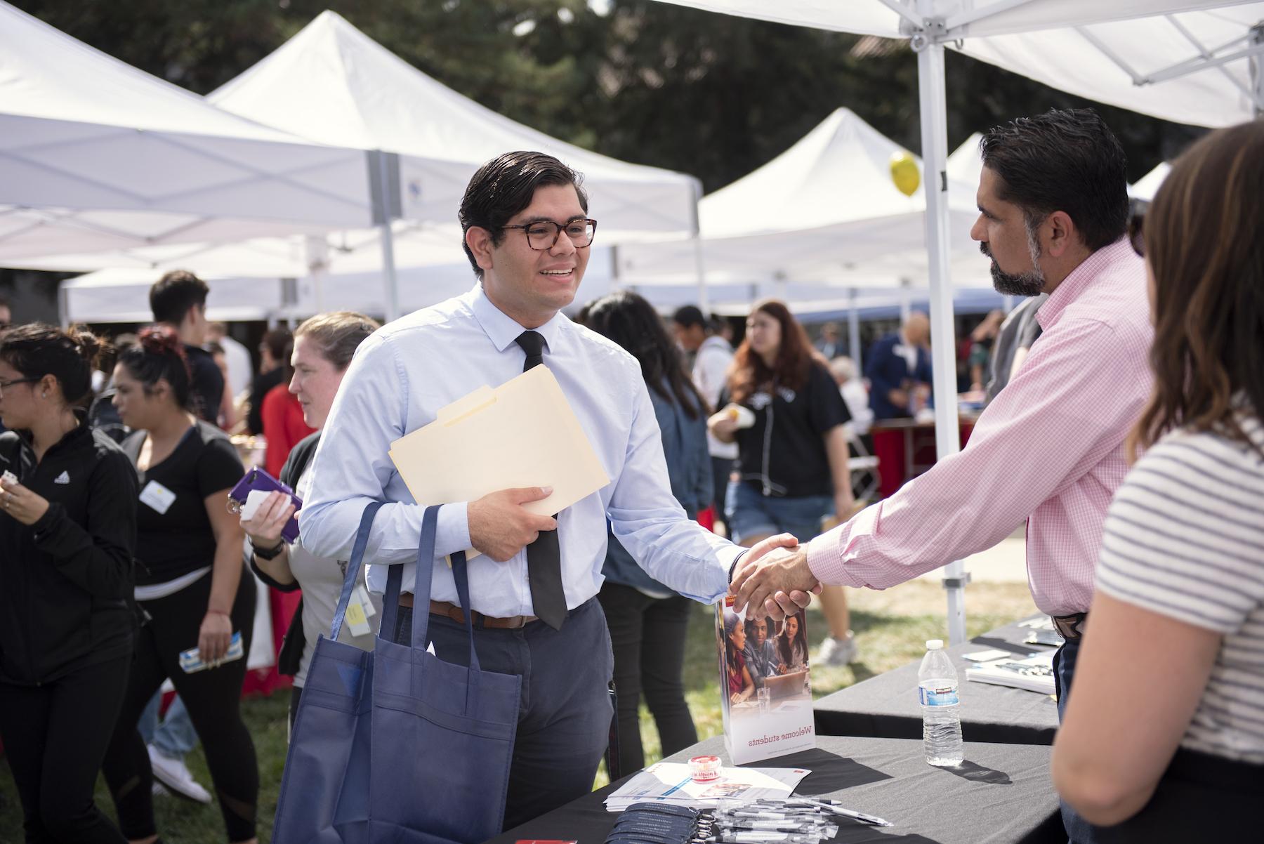 A student in a tie smiling and shaking hands with a man