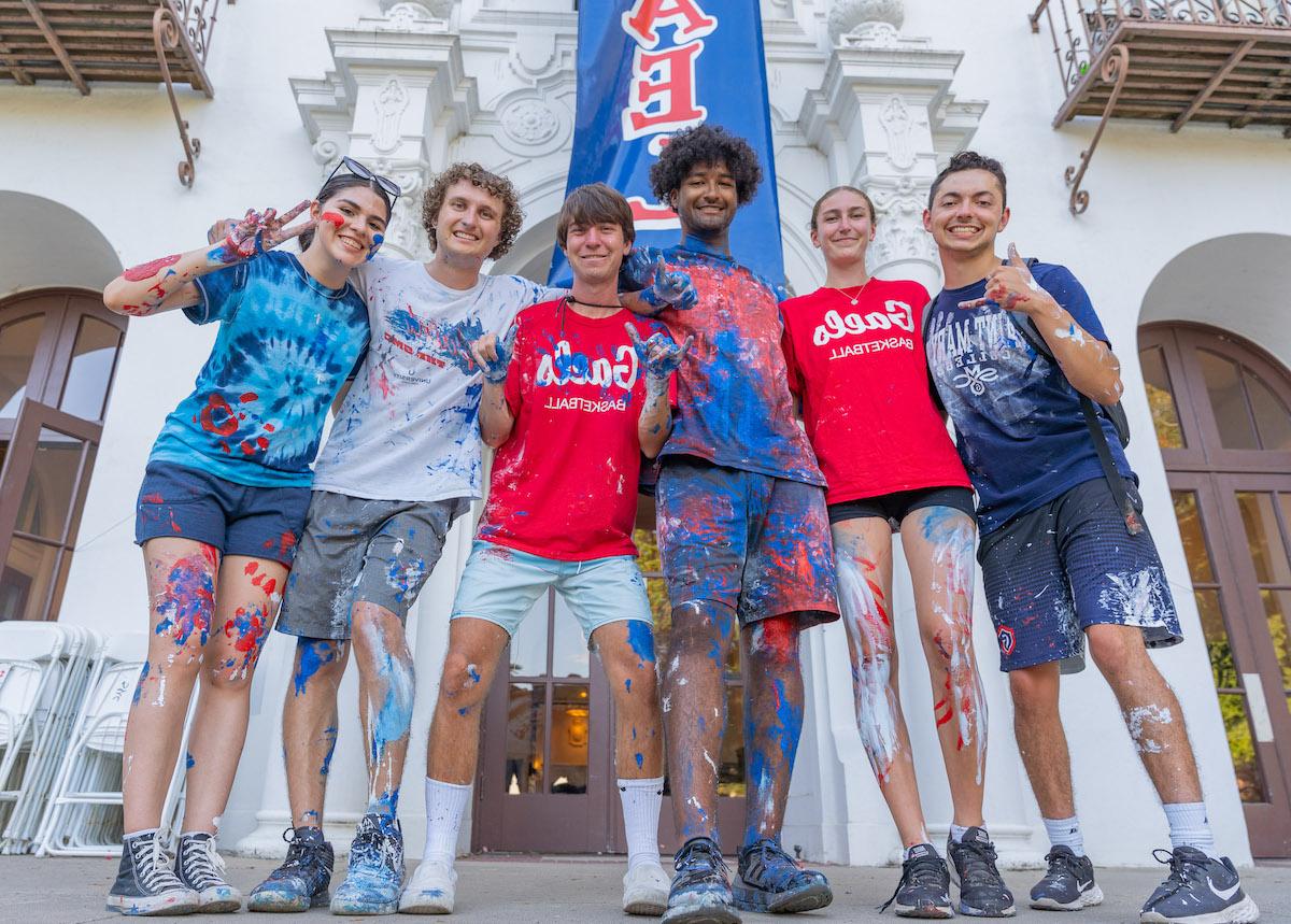 Six students covered in paint in front of the sign GOD IS A GAEL