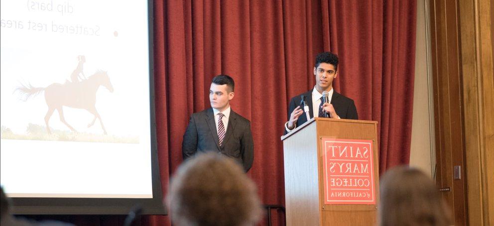 Students on stage in suits presenting at a Business Administration Case Competition