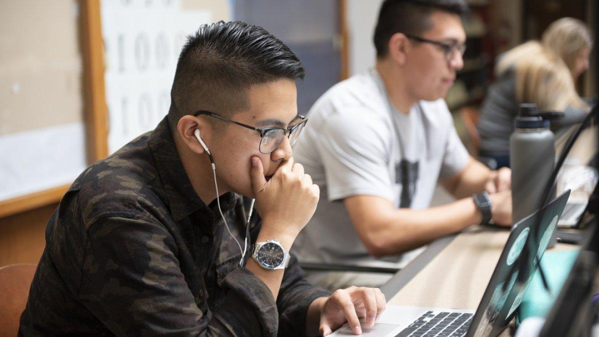 A student working on a computer with ear buds in 